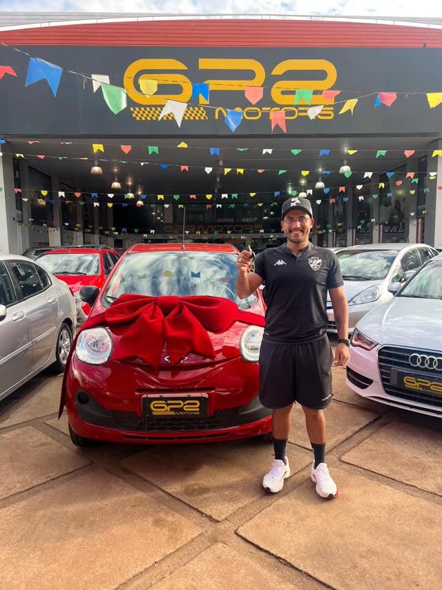 Cliente da +Rating na loja de veículos, ao lado do carro novo com laço vermelho
